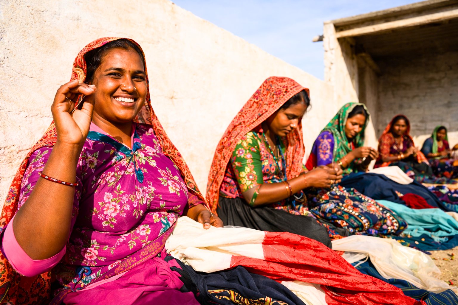 Women of different ages working together on handcrafted textiles, one smiling at the camera